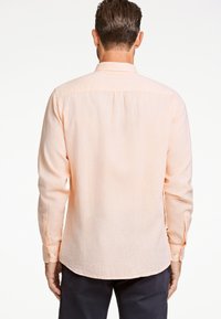 Camisa de manga larga color durazno claro con un acabado texturizado, puños abotonados y un detalle de pliegue en la parte posterior. Diseño de cuello clásico y dobladillo curvado.