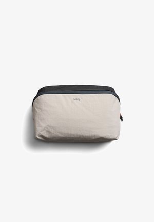 Kompakte beige-schwarze Reißverschlusstasche mit minimalistischem Design und „bellroy“-Logo auf der Vorderseite, präsentiert vor weißem Hintergrund.