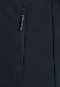 Dark blue, smooth fabric with a zippered pocket featuring a metallic pull tab, stitched neatly with a slim, tailored design.