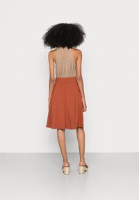 Top a halter marrone con righe verticali abbinato a una gonna abbronzata lunga fino al ginocchio. Entrambi i capi presentano una texture liscia e morbida.