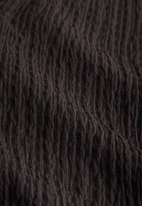 Tissu marron foncé avec une surface texturée froissée, montrant des crêtes verticales et des plis doux.