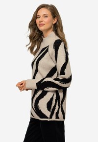 Beige Pullover mit schwarzem Zebra-Streifenmuster, gerippter Kragen und Bund, lockere Passform, weiche Strickstruktur, seitliche Schlitze für mehr Bewegungsfreiheit.