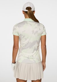 Jasnozielona polo z wzorem w delikatne zygzaki, zestawiona z plisowaną beżową spódnicą. Koszulka ma krótki rękaw i kołnierzyk.