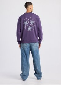 Paarse trui met een cirkelvormig grafisch ontwerp op de achterkant. Gecombineerd met losse blauwe spijkerbroeken, voor een casual silhouet.