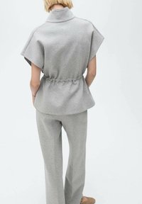Ensemble en sweat-shirt et pantalon gris avec un col montant, des manches courtes et une taille froncée pour la mise en forme. Texture douce et lisse.