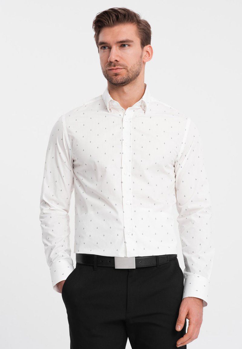 Camisa blanca de botones con pequeños patrones de anclas en navy, de manga larga y con cuello. Se lleva con pantalones negros y un cinturón negro.