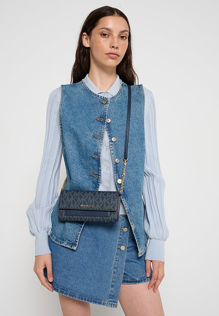 Gilet di jeans blu con chiusure a bottone indossato sopra una maglietta a righe blu chiaro. Piccola borsa a tracolla in tessuto scuro a motivo con tracolla in oro.
