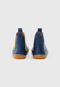 Botas de piel azul hasta el tobillo con paneles laterales amarillos, textura suave, punta redondeada y suelas de goma marrones. Tiradores traseros para facilitar el calzado.