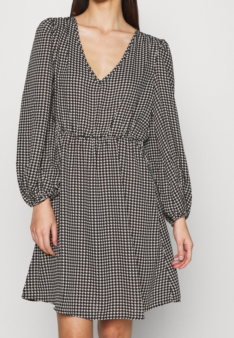 Svart- och vittmönstrad klänning med V-ringning, långa puffärmar och elastisk midja, med en utsvängd kjol och houndstooth-design.
