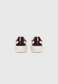 Sneaker eleganti con una base bianca e accenti lucidi di un bordeaux scuro, forma arrotondata, superfici texturizzate e una robusta suola color crema.