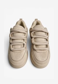 Krém színű sneaker, puha nubukból készült, hat fűzőlyukkal, párnázott bokarésszel, perforált lábujjrészsel és lapos gumitalppal. Fentről nézve.