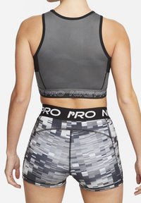 Grå sportsbh med tekstureret mønster; elastisk bånd mærket "NIKE PRO." Sorte og grå mønstrede shorts med kontrasterende syninger, hvor logoet er placeret på livet.