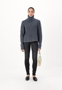 Szürke, bordázott garbós pulóver hosszú ujjakkal, sötét skinny farmernadrággal és fekete slip-on cipőkkel párosítva. Továbbá van rajta egy krémszínű kézitáska.