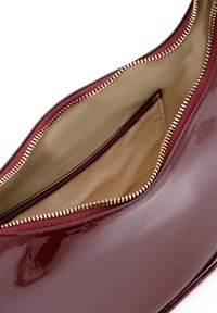 Bordeaux patentleren handtas met een gouden rits, met een gladde buitenkant en een beige stoffen gevoerd interieur met een klein vakje.