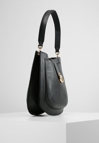 Czarna skórzana torebka o zakrzywionym kształcie, płaskim dnie, złotych elementach ozdobnych i pojedynczym uchwycie u góry do noszenia.