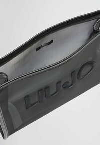 Črna kozmetična torbica iz mrežastega materiala, opremljena z zadrgo in izbočenim logotipom "LIUJO" na sprednji strani. Teksturna površina z gladkim robom.