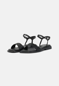 Sandali neri con design open-toe, multiple cinghie, sole piatta e fibbia regolabile alla caviglia per una vestibilità sicura. Realizzati in pelle.