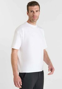 T-shirt bianco a maniche corte realizzato in tessuto di cotone liscio, con una vestibilità ampia e scollatura rotonda, abbinato a pantaloni neri.