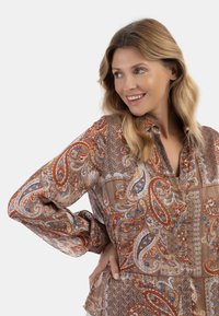 Blusa marrone con motivo a paisley e dotato in arancione e blu, con maniche lunghe e chiusura con bottoni.