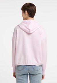 Lichtroze hoodie met een trekkoordcapuchon, geribde manchetten en zoom. Zachte textuur, relaxte pasvorm, gedragen met lichtblauwe jeans. Achteraanzicht.