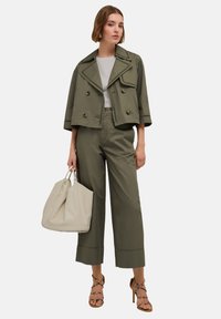 Olijfgroene cropped jas met dubbele knopen, gecombineerd met hoogzitende wijde broeken en een beige tas. Sleehak sandalen met bandjes.