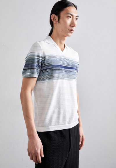 Λευκό κοντομάνικο πόλο μπλουζάκι με μ�πλε οριζόντιες ρίγες, σχέδιο με V-λαιμόκοψη, υφή πλεκτού, συνδυασμένο με μαύρο παντελόνι με σχέδιο.