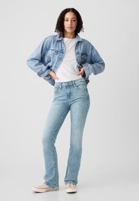 Lichtblauwe spijkerjas met een losse pasvorm, gecombineerd met lichtblauwe jeans. De jeans is slim-fit, en beide kledingstukken hebben een klassiek design.