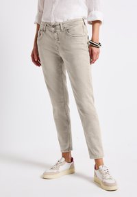 Light gray denim jeans with a slim fit, five pockets, and subtle stitching details, paired with white and beige sneakers.
