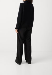 Maglione lavorato a maglia nero con collo alto, abbinato a pantaloni neri a gamba larga. Presenta una texture a coste e gambe dei pantaloni ampie.