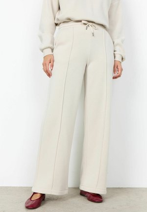 Béžové široké nohavice s prednými švami a sťahovacou šnúrkou v páse, nosené s rovnakou mikinou a červenými plochými topánkami.