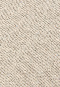 Tessuto testurizzato con un motivo a spina di pesce beige e bianco. Il materiale ha un aspetto tessuto con una leggera lucentezza.