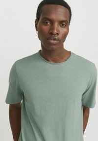 Light green short-sleeve t-shirt made from soft material, featuring a round neckline with raw edge detail and a relaxed fit.