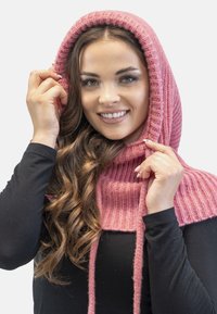 Cappuccio lavorato a maglia di un rosa chiaro con texture a coste e stringhe. Abbinato a una maglietta nera a maniche lunghe, realizzata in materiale morbido e flessibile.
