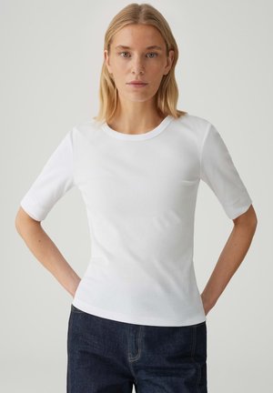 T-shirt blanc côtelé à manches courtes avec un col rond, design ajusté et texture lisse, associé à un jean en denim bleu foncé.