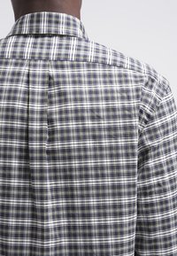 Camisa de cuadros con un patrón a cuadros en navy, blanco y amarillo. Presenta un cuello clásico y un pliegue en la parte posterior para un ajuste relajado.