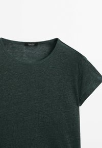Donkergroene t-shirt met korte mouwen en ronde hals, gemaakt van zachte, gestructureerde stof. Bevat een subtiel merkembleem op de hals.