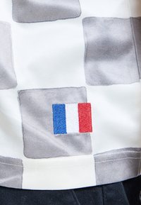 Tissu à carreaux gris et blanc avec un petit drapeau français brodé en carrés bleu, blanc et rouge près du bord inférieur.