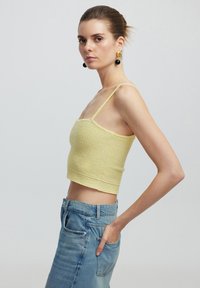 Top corto amarillo texturizado con tirantes finos, combinado con jeans de mezclilla azul claro. Diseño simple con un dobladillo elástico.
