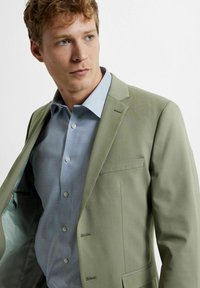 Light green suit jacket with a notch lapel, single button closure, and a chest pocket, layered over a light blue button-up shirt.