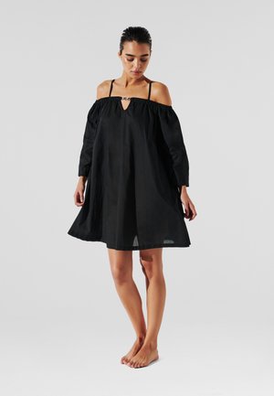 Schwarzes Off-Shoulder-Kleid mit langen Ärmeln, das einen Schlitz-Ausschnitt und eine fließende Silhouette aufweist, aus leichtem Baumwollstoff gefertigt.