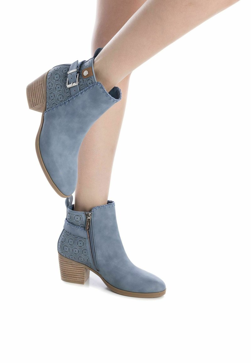 Bottines bleu clair avec un design perforé, fermeture éclair sur le côté et un talon en bois massif. Présente des accents cousus sur le dessus et le talon.