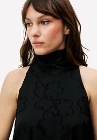 Zwart mouwloos topje met een hoge hals, voorzien van een gestructureerd bloemmotief. Gladde stof met een subtiele glans en een aansluitende pasvorm.