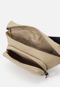 Beige keresztpántos táska sima szintetikus anyagból, cipzáros záródással, két rekesszel és fekete állítható pánttal. A belső tér szövetbéléssel rendelkezik.