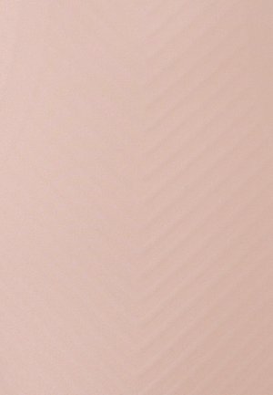 Femme en blazer beige tenant un sac à main en cuir sur l'épaule, debout devant un fond blanc uni.