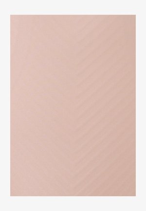 Femme en blazer beige tenant un sac à main en cuir sur l'épaule, debout devant un fond blanc uni.