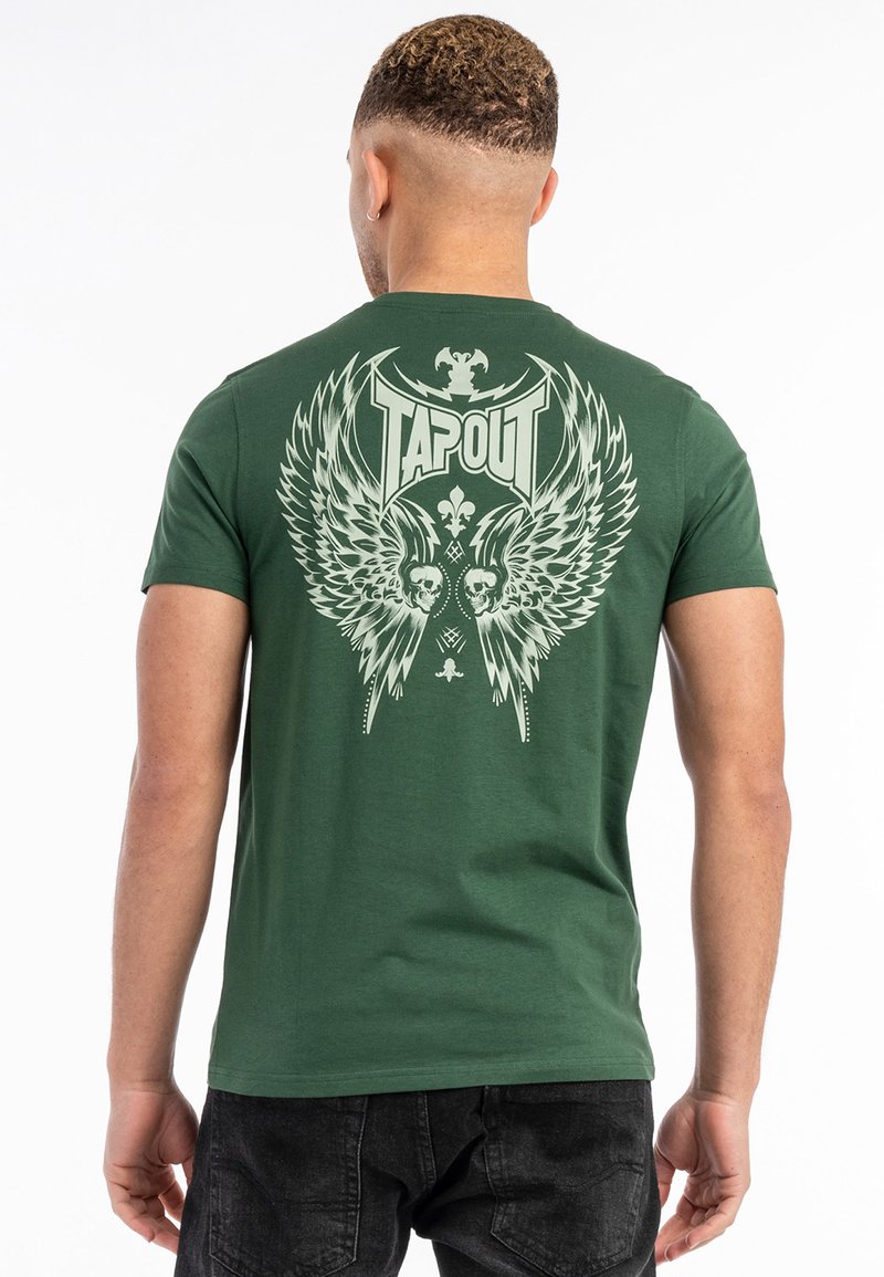 Zaļš kokvilnas T-krekls ar lielu balto grafiku, kas satur spārnus un galvaskausa akcentus, un logo "TAPOUT" treknā burtveidā uz muguras.