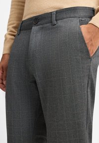 Grijze broek met visgraatpatroon en een subtiele oranje ruitdetail, met een vlakke voorkant, twee zijzakken en een enkele knoopsluiting.