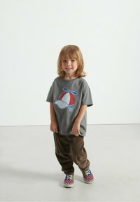 Hallhalline t-särk sinise ja punase trükitud propelleri mütsiga, millele on sobitatud pruunist kootud püksid ja mitmevärvilised ruudulised tossud.