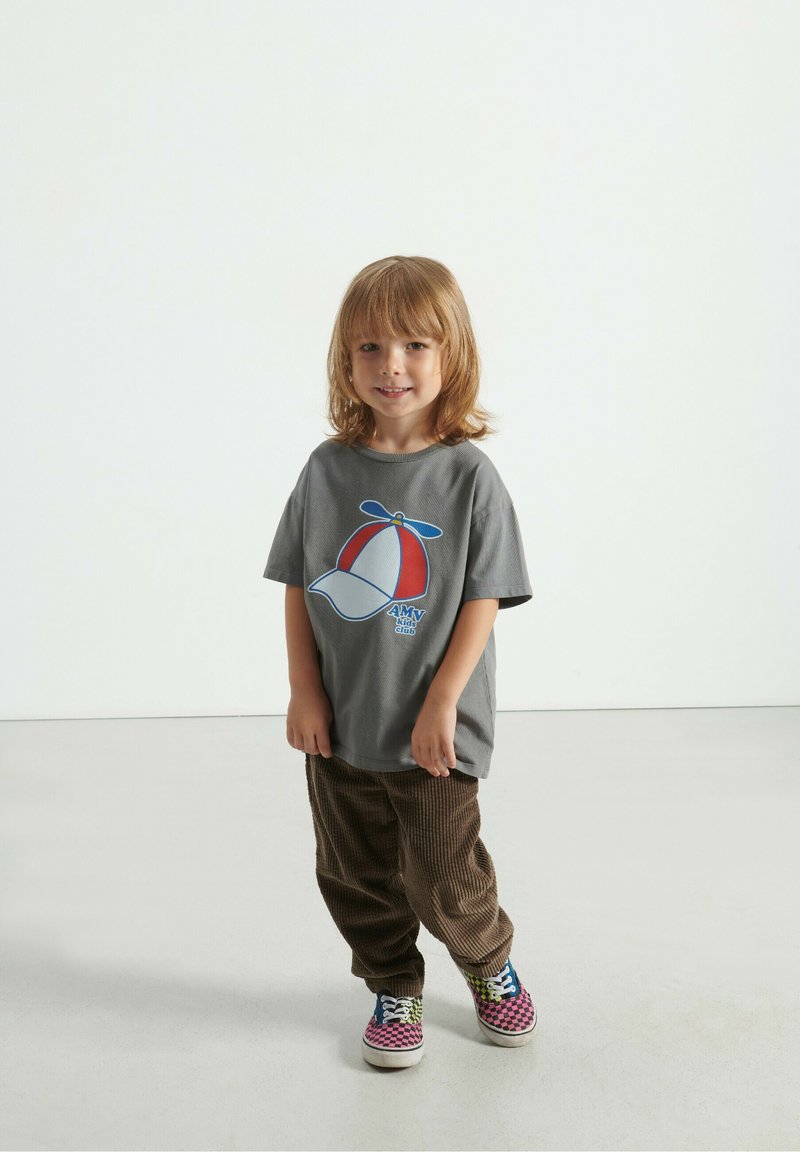 Hallhalline t-särk sinise ja punase trükitud propelleri mütsiga, millele on sobitatud pruunist kootud püksid ja mitmevärvilised ruudulised tossud.