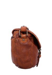 Bruine leren crossbodytas, zijaanzicht met zichtbare metalen gesp en klepsluiting tegen witte achtergrond.